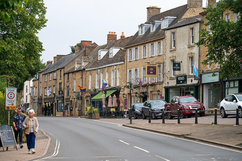 Beige coloured shops line a picturesque high street in the Cotswolds.