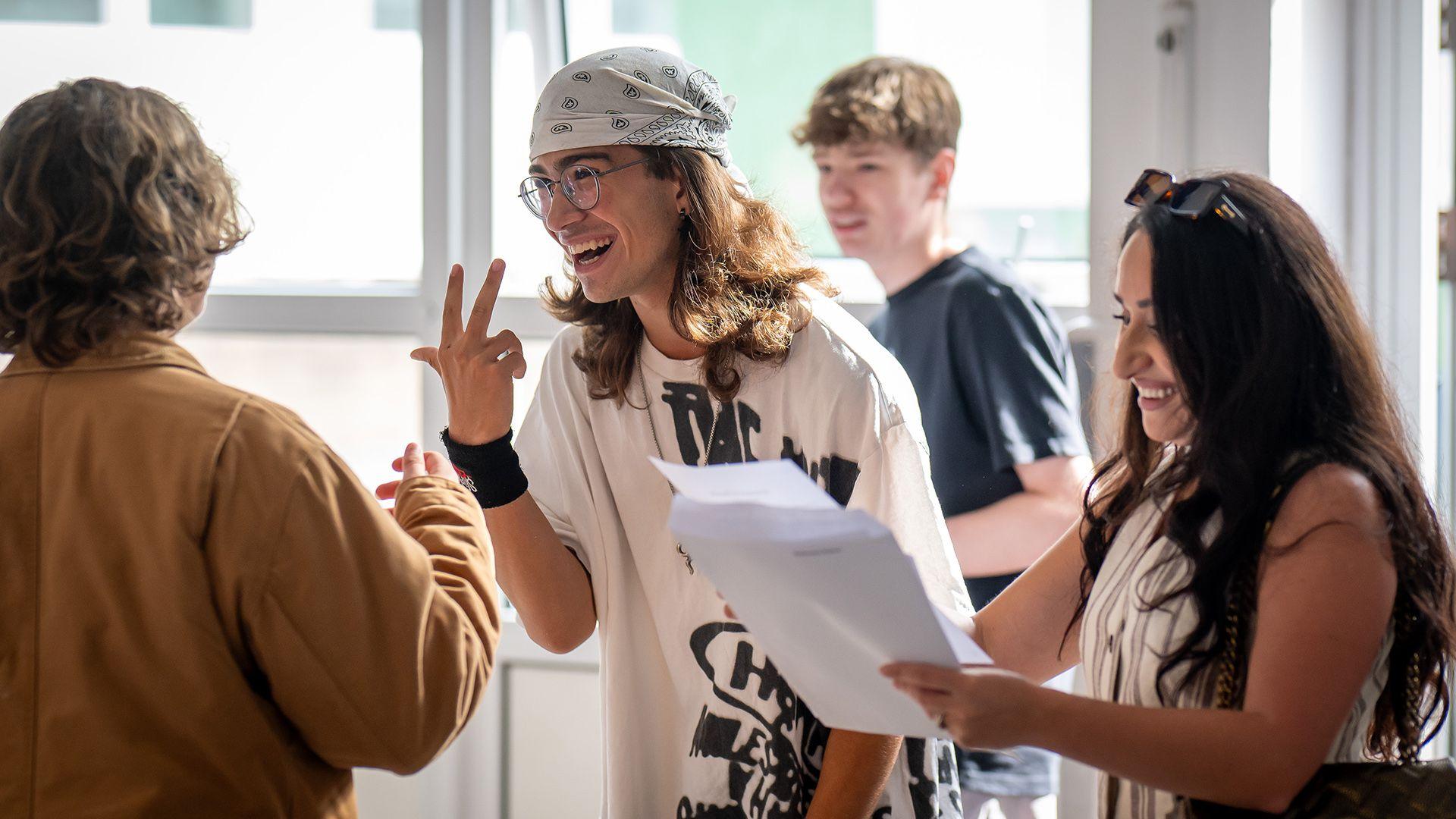 A group of students gather around holding papers and gesturing to each other while reading their results at a high school in Cardiff on Thursday.