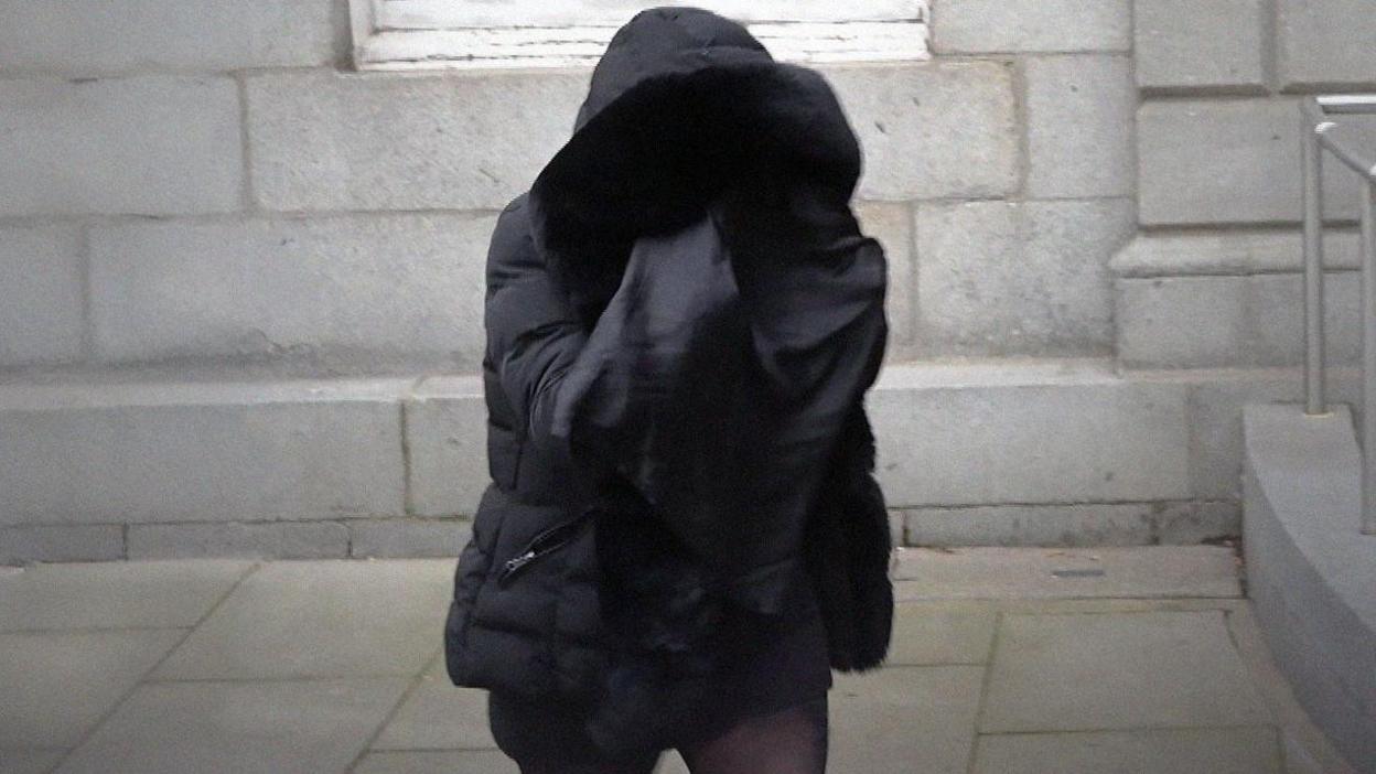 A person wearing a parka walks outside a court building covering her face in a black material