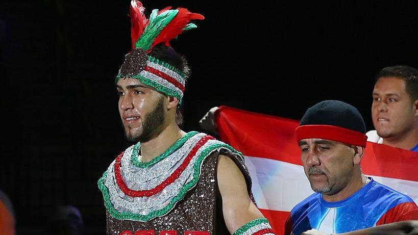 Prichard Colon wears a sparkly red, silver and green vest and headband with feathers