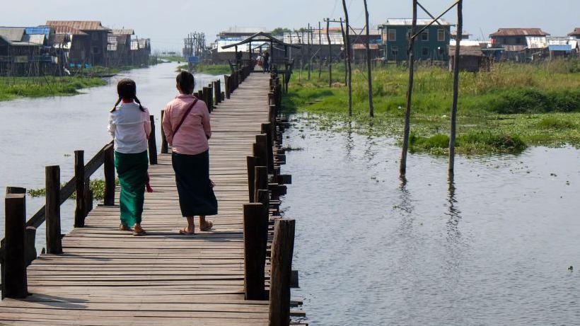 Two girls viewed from behind walking on a footbridge in the village of Mang Thawk, Inle Lake