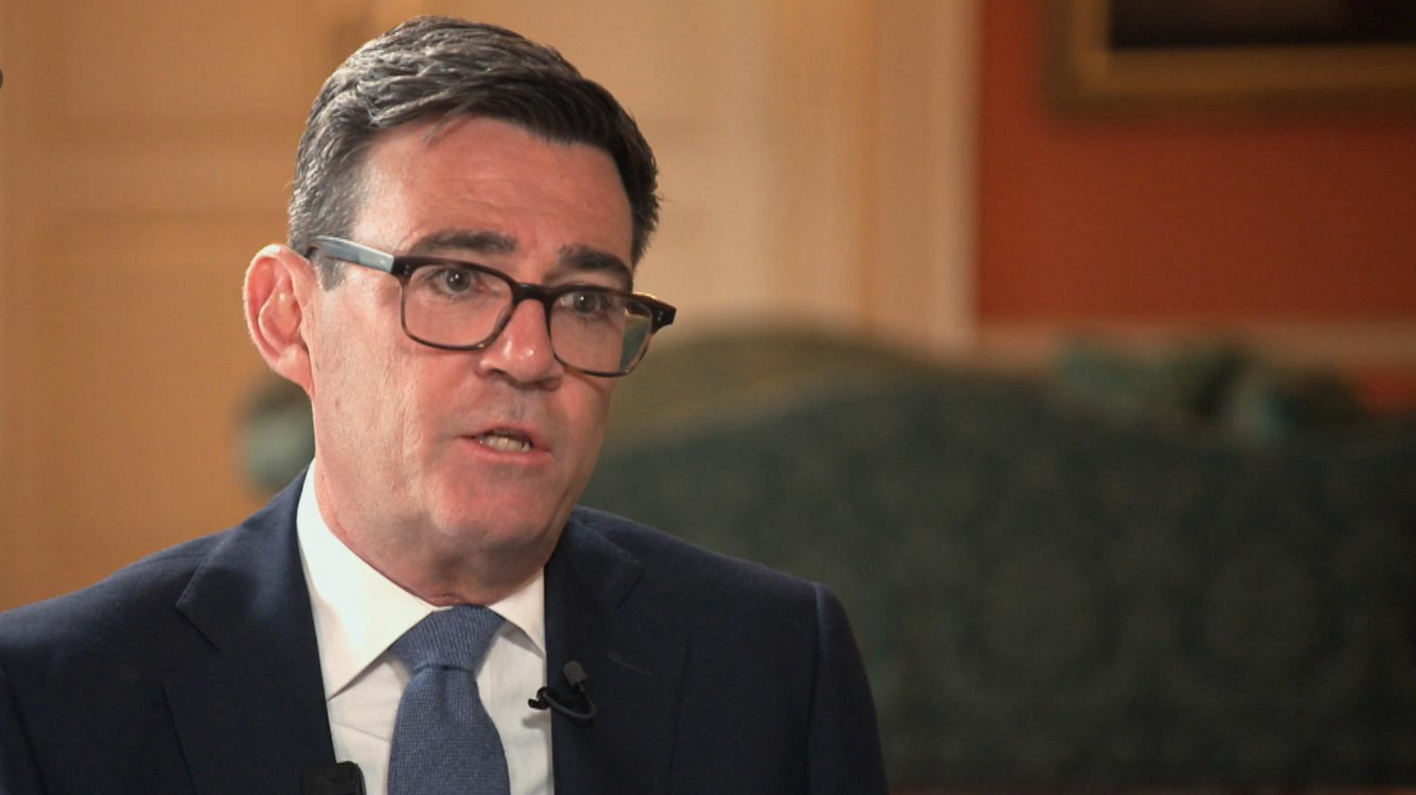 Andy Burnham, wearing glasses, a suit jacket and a blue tie, speaks