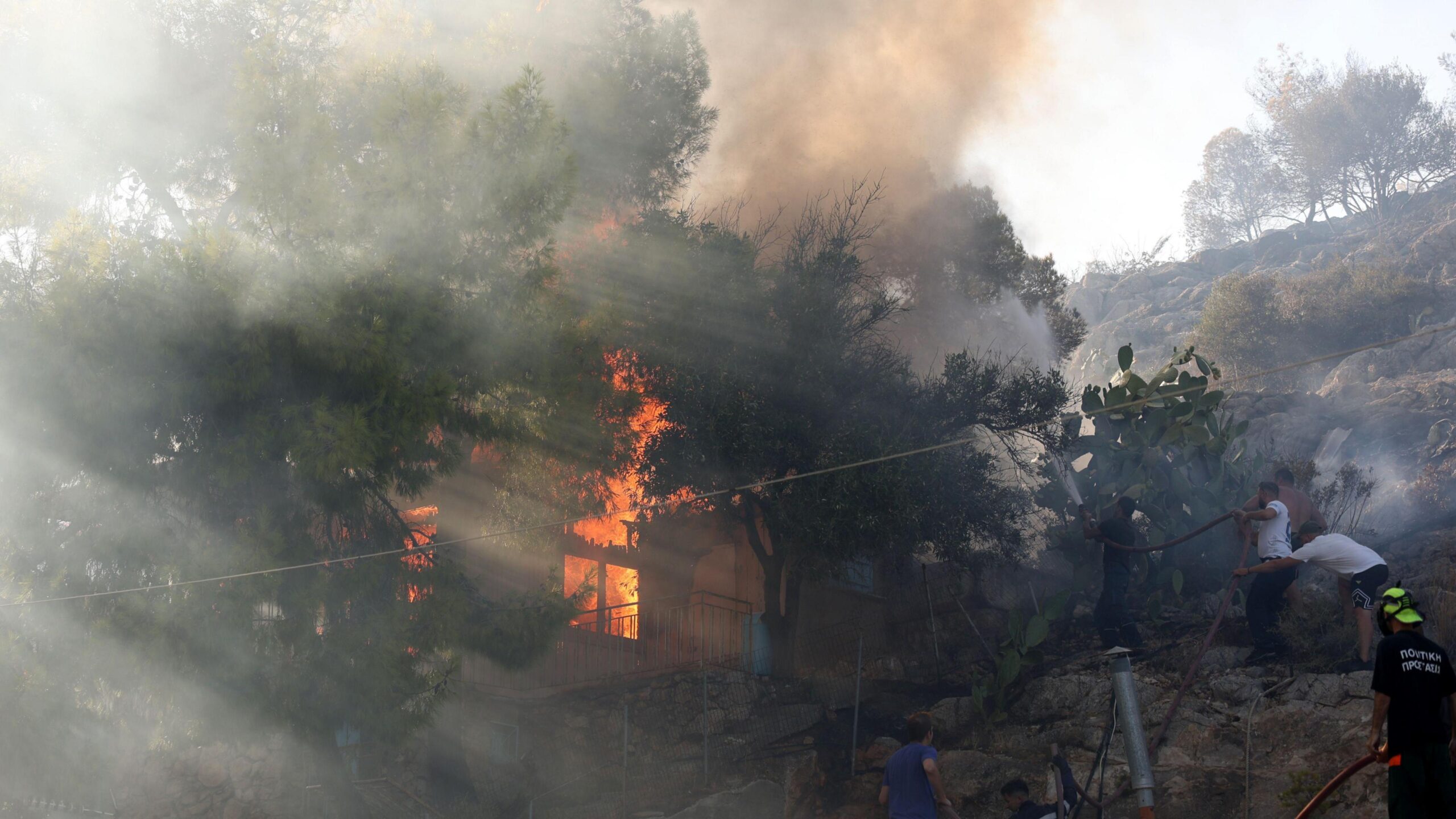 Flames and smoke billow from a burning house in Peristeria as firefighters and volunteers work to extinguish the blaze on Salamina Island