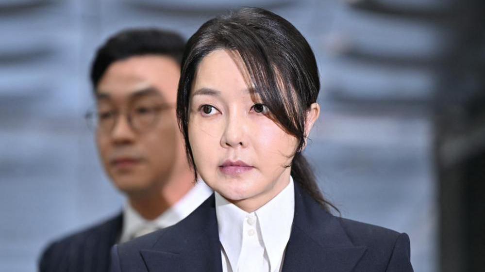 Kim Keon Hee, in a white dress suit and black blazer, arrives in court in Seoul to attend a hearing