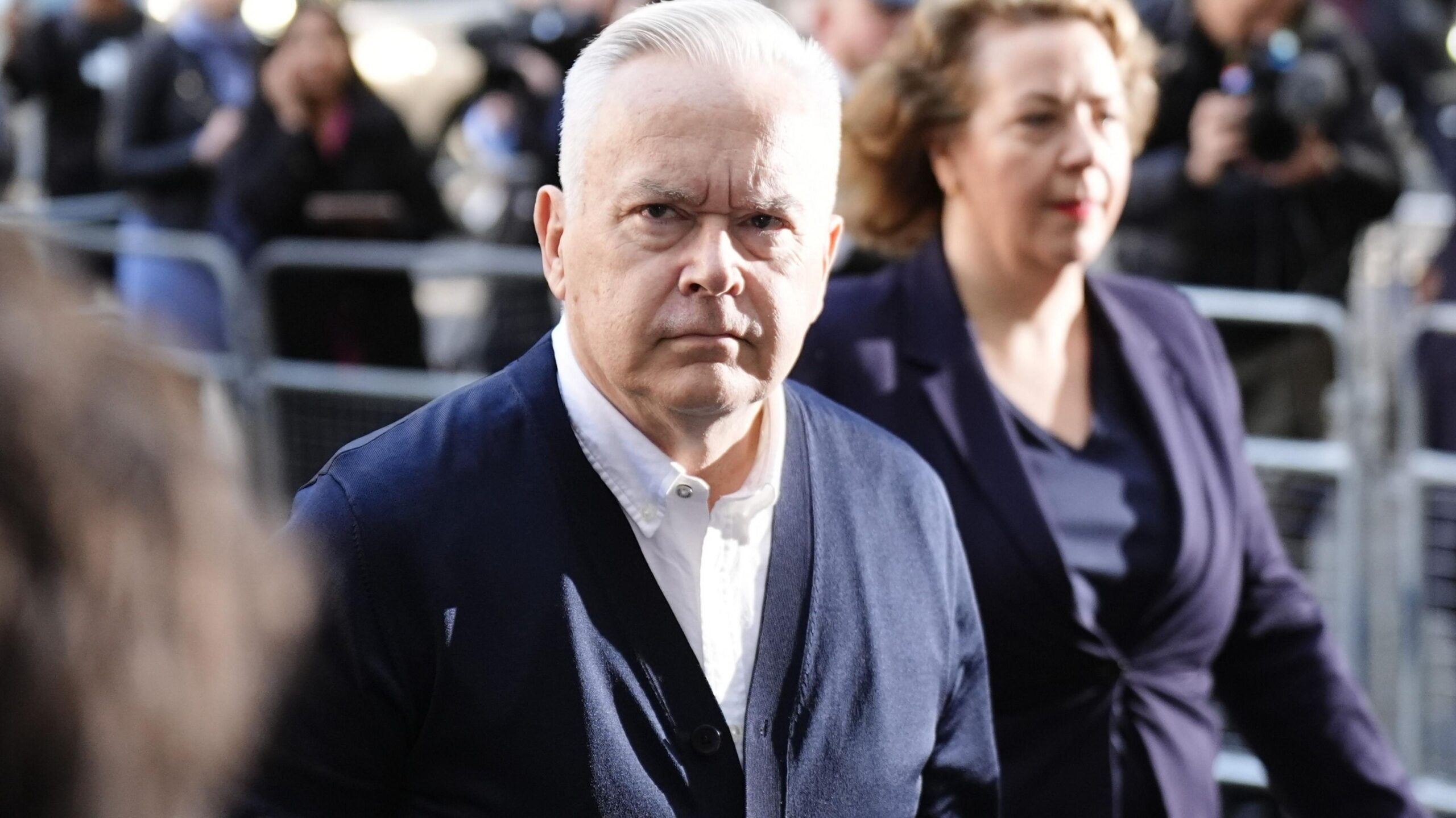 A man with grey hair, tanned skin, wearing a white shirt and blue jacket