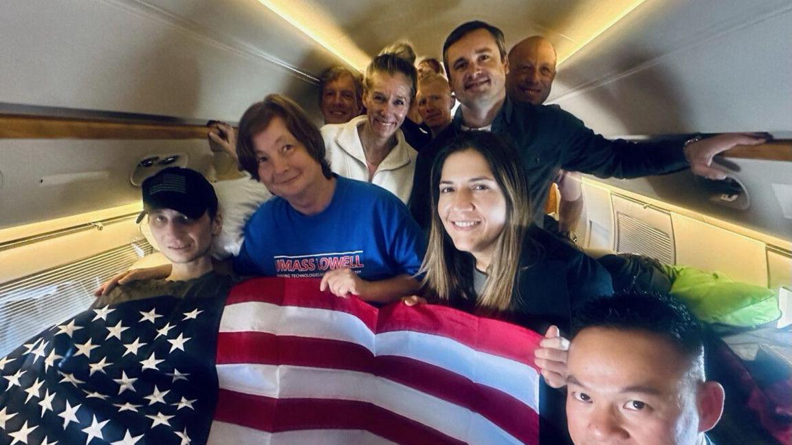 Gilman, left, seen with an American flag draped over him on the plane. He is beside several other people, including his mother