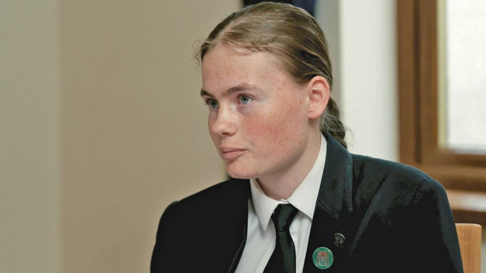 Bethany speaks to the BBC while wearing her school uniform, which includes a dark blazer with a green pin-on badge.