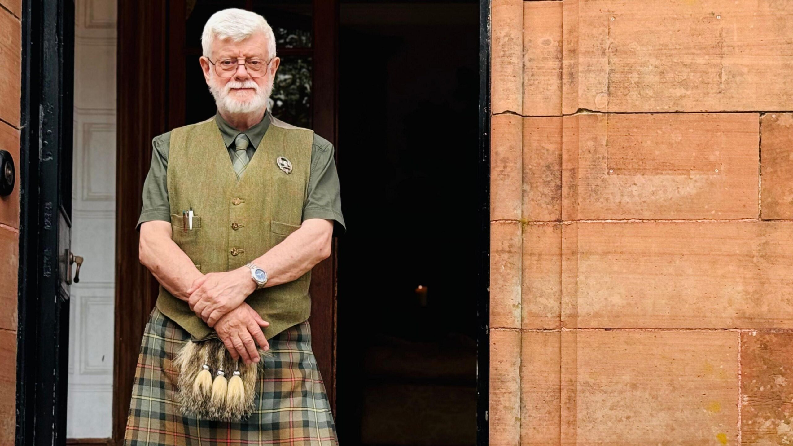 James MacLeod, concierge at the Glencoe House Hotel, stands outside the entrance, wearing traditional Scottish attire, including a kilt