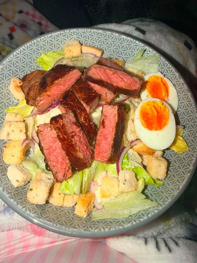 A plate with sliced cooked steak, boiled eggs, croutons and lettuce