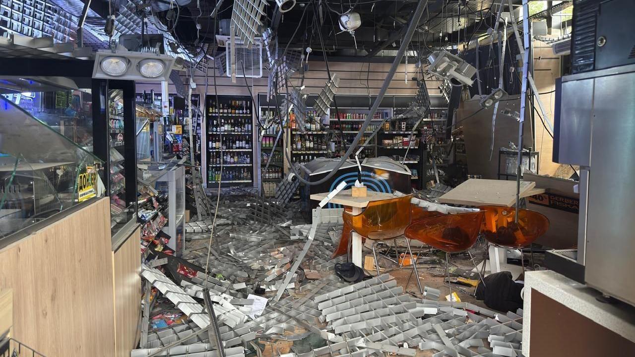 The inside of a petrol station is destroyed by a Russian attack. Wires hang from the roof and shelves and debris are strewn all over the floor