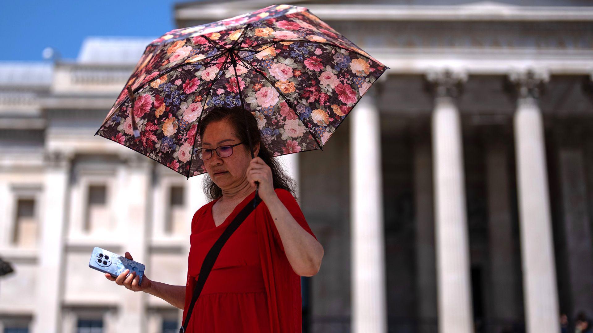 A woman with a flower-coloured umbrella walks in the sun