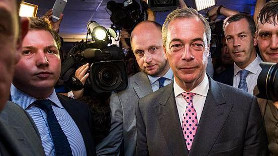 Nigel Farage arrives at the Leave.EU campaign's referendum party in 2016. To his far-right is George Cottrell wearing a light blue shirt and navy tie.
