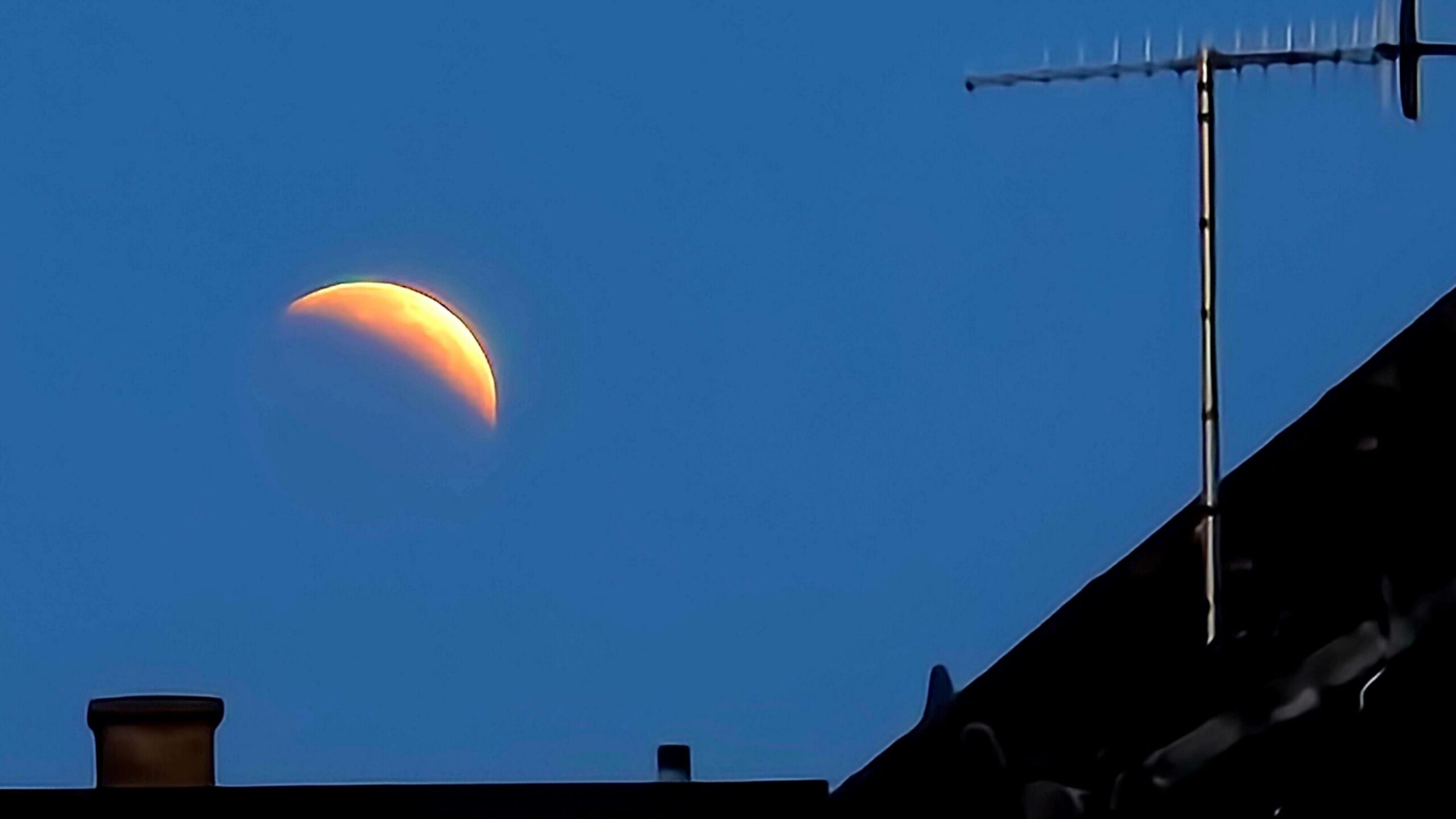 Roof tops and tv aerial with the crescent of the partially eclipsed moon above