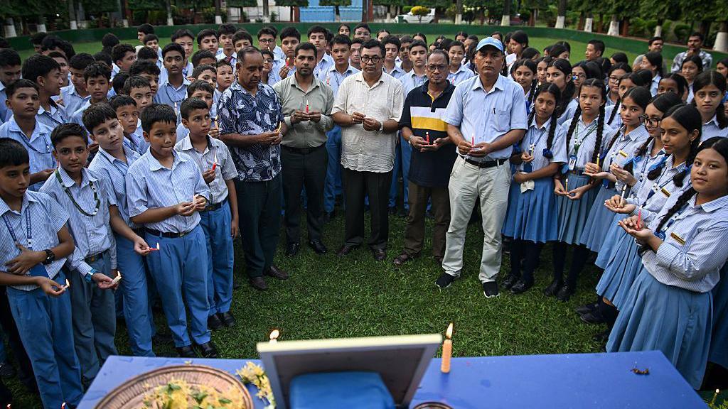 Students and a few men hold candles and stand around a blue table