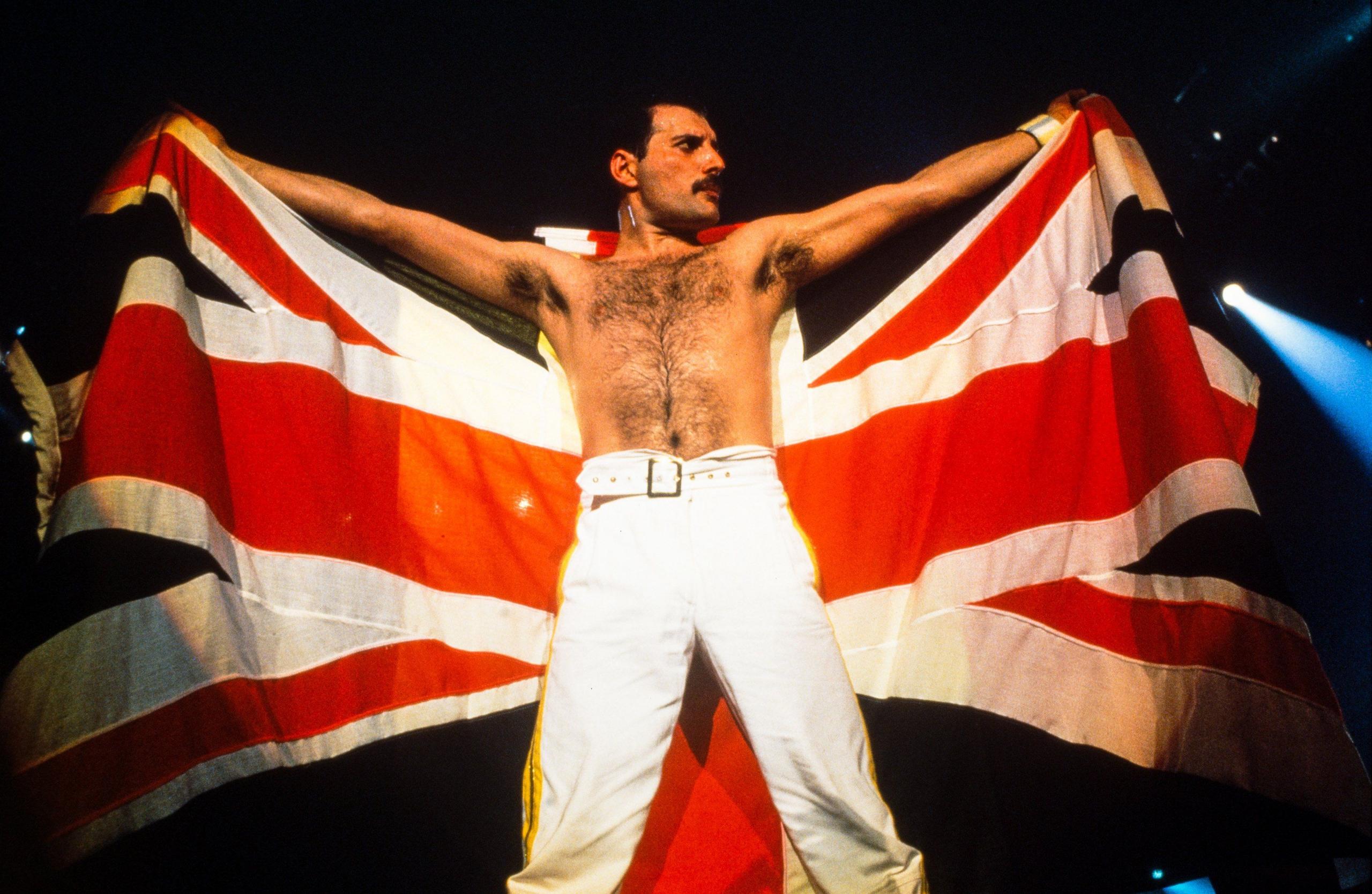 Freddie Mercury, shirtless on the Knebworth stage, is holding a Union Jack behind him