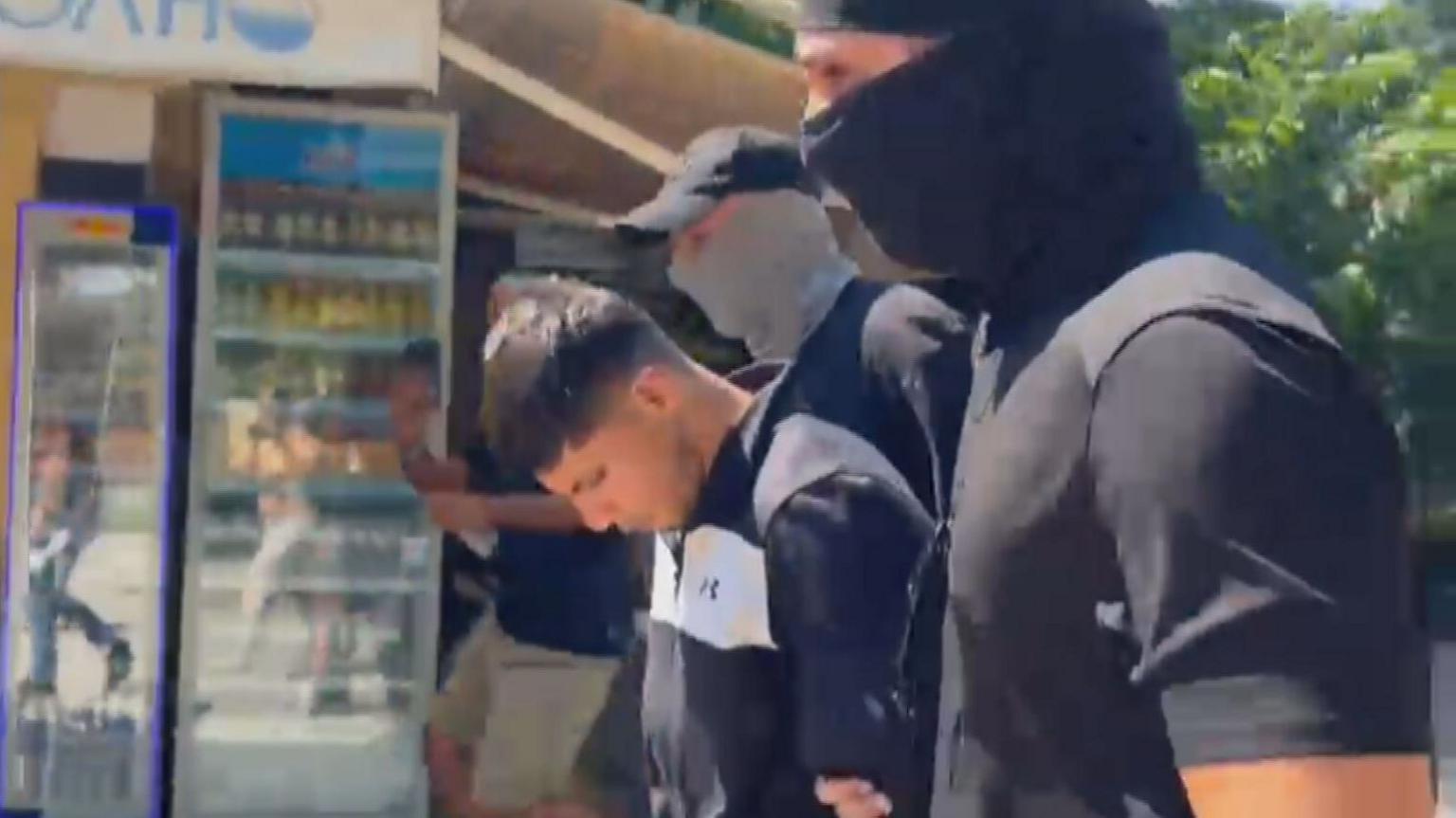 Sharif Ahmadzai leaving the court between two men dressed in black with face coverings, who are holding his arms.