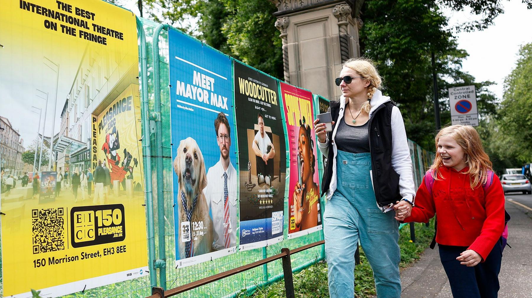A woman and child walk past colourful posters for the Edinburgh Fringe festival on a street in Edinburgh