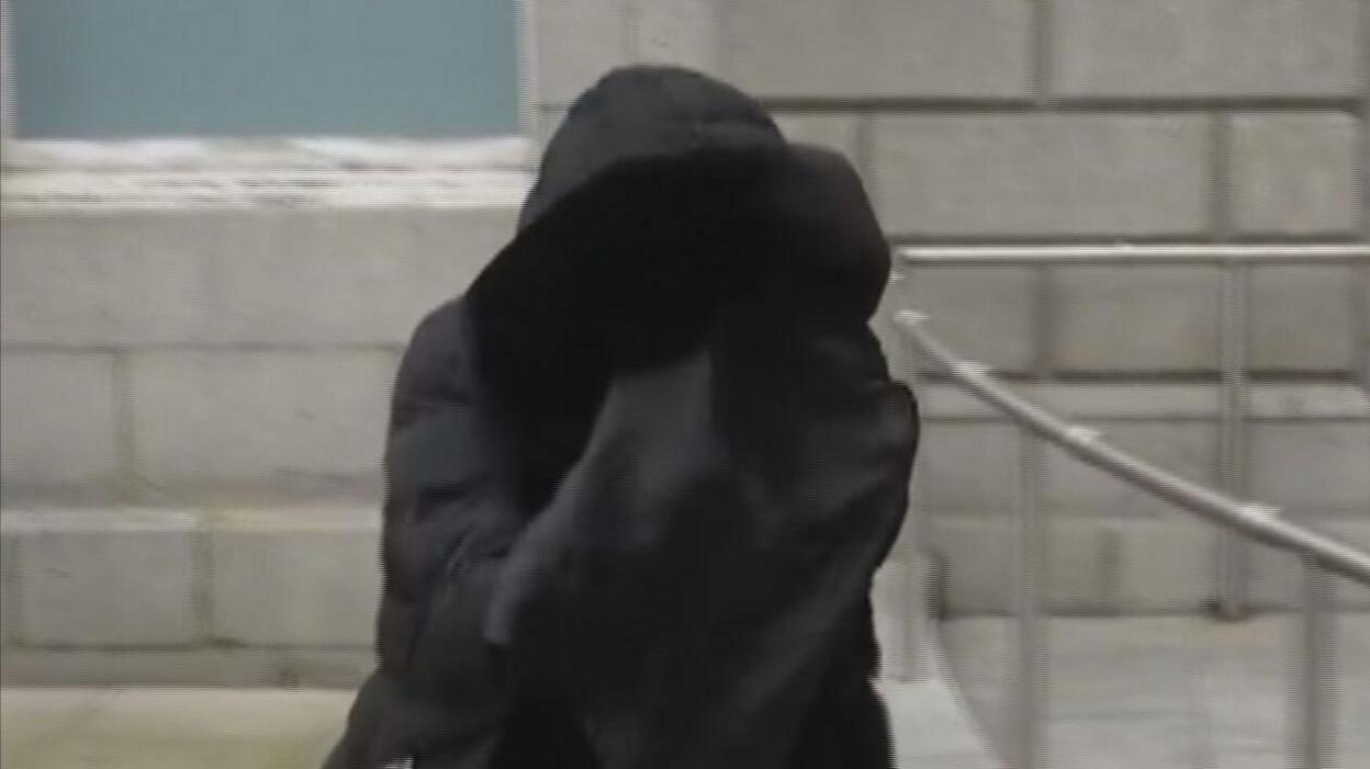 A person wearing a parka walks outside a court building covering her face in a black material