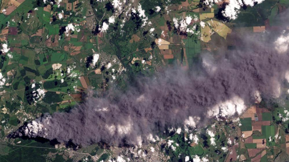 A satellite shows dark smoke coming from a small area and billowing out to cover a large area of countryside
