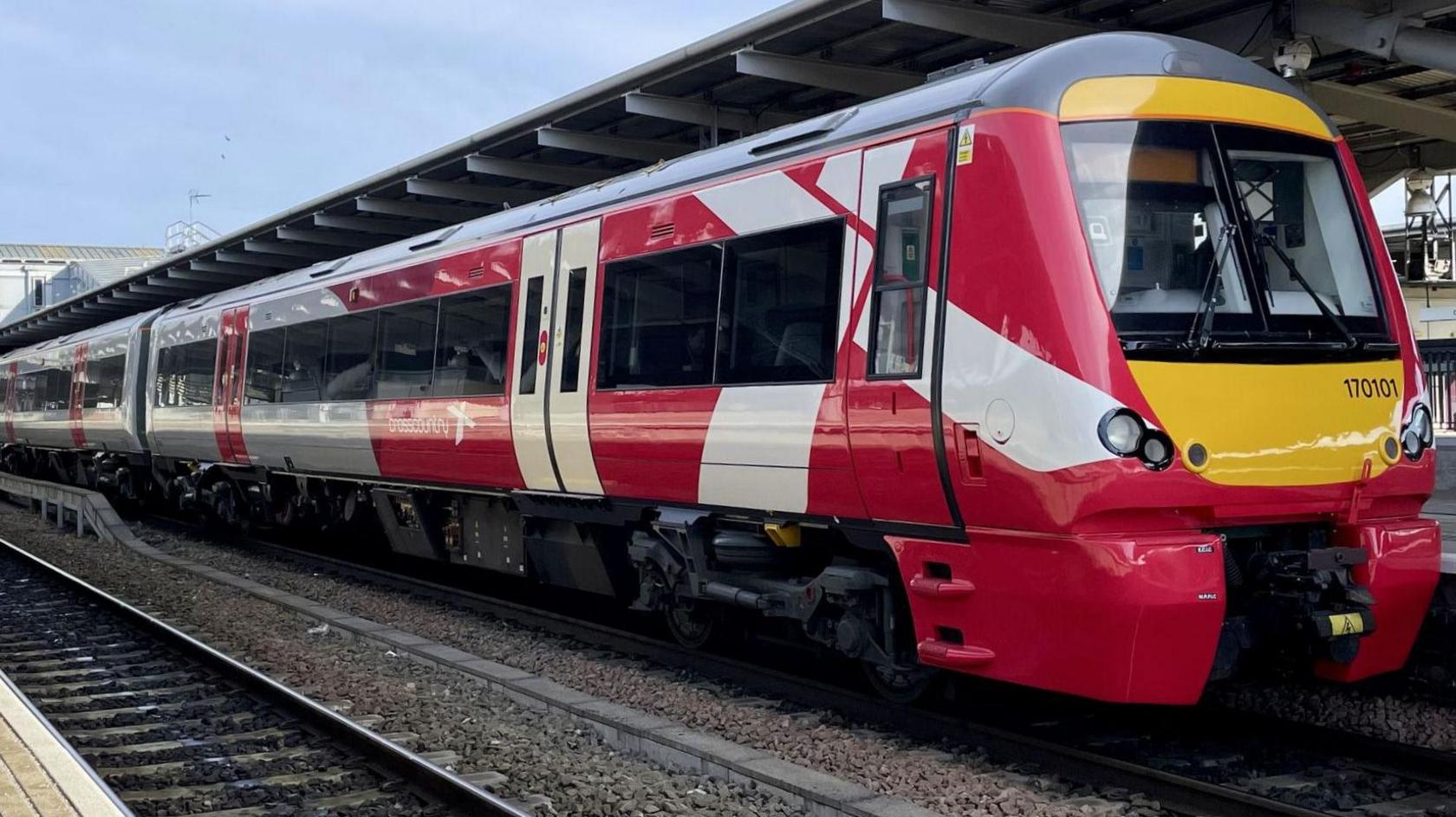 A red and white train is parked on railway tracks next to a train station.