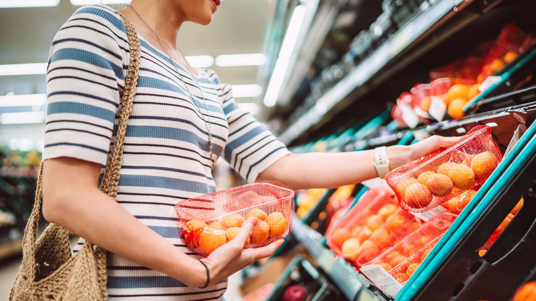 A woman in a stripey top inside a supermarket looking at fruit and picking up nectarines