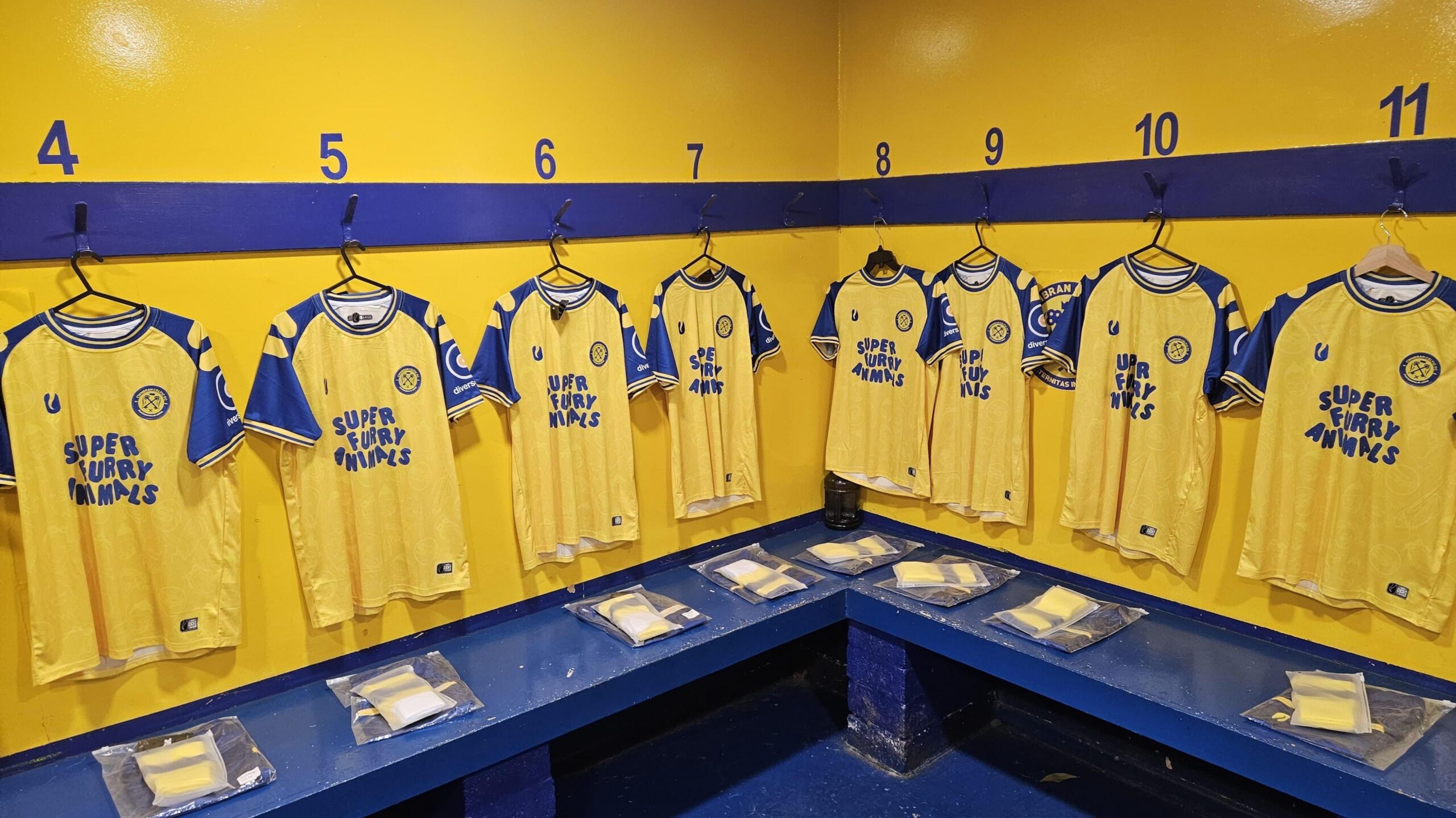 Team shirts hang in the men's changing rooms, yellow in colour with blue sleeves and blue writing on the front saying Super Furry Animals.