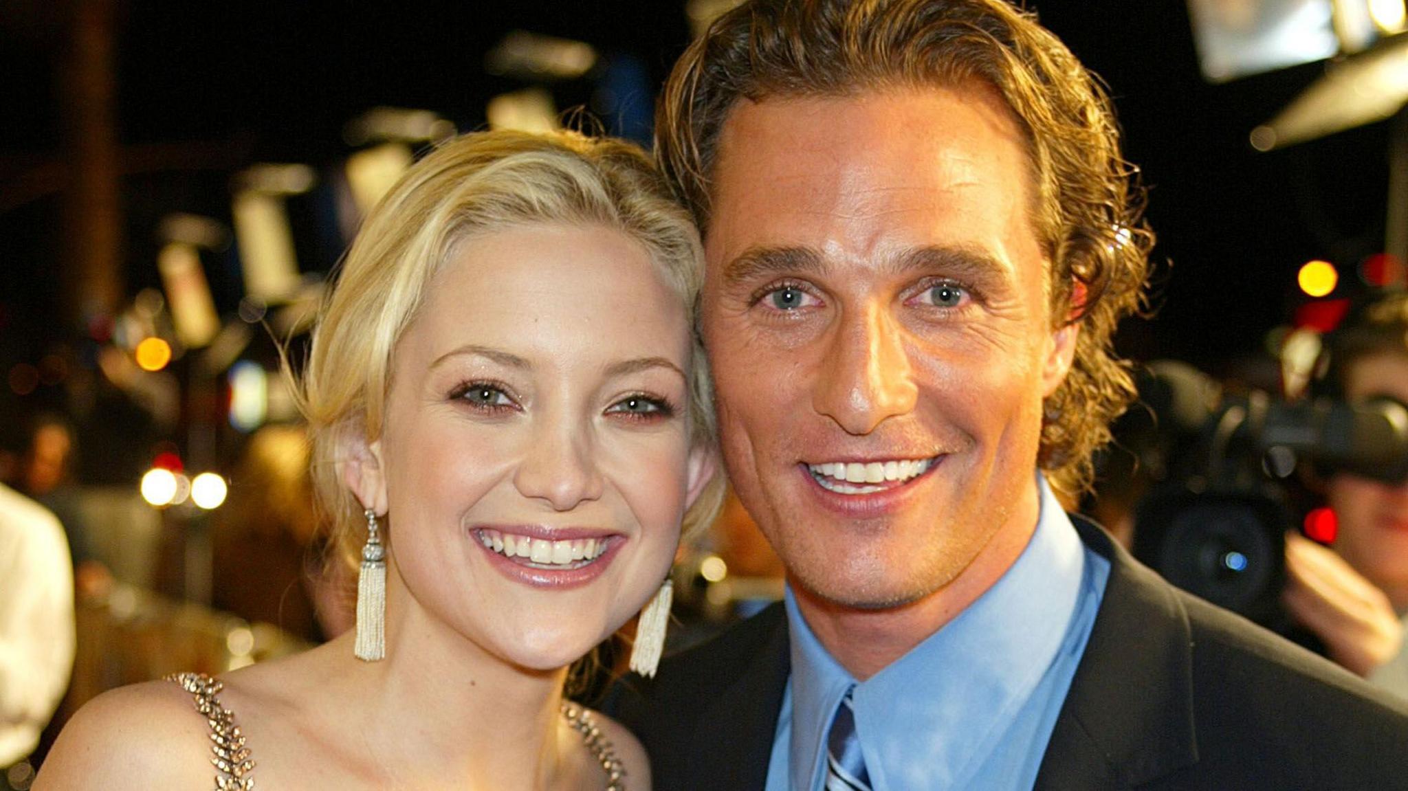 Kate Hudson and Matthew McConaughey standing together and smiling in formal dress, with red carpet activity behind them