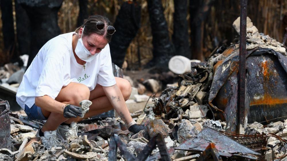 Julie inspects the debris of her parents' home after it was destroyed by a wildfire in Le Porge