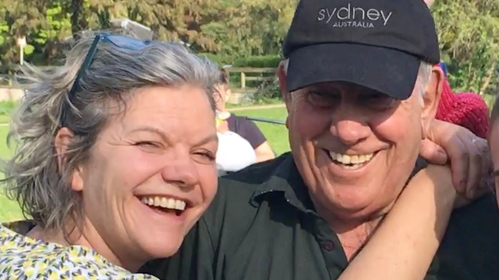Rebecca holds her arms around her dad's shoulders. Both smile at the camera, it is a head and shoulders shot of them both. Bob wears a black cap and black polo shirt, Rebecca has chin length wavy hair, with her glasses perched on top of her head.