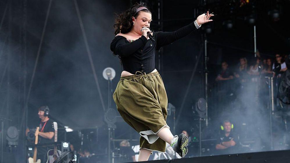 Lola Young on stage in green trousers and a black top