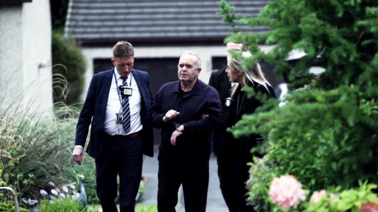 A handcuffed 77-year-old man is led from his house by two police officers