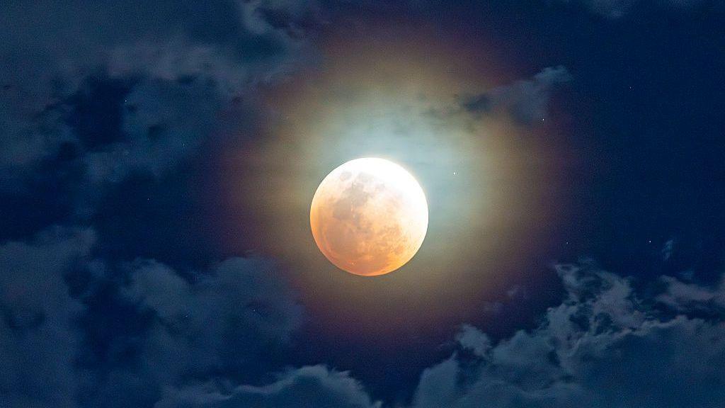 Image of Moon with reddish tinge in cloudy skies