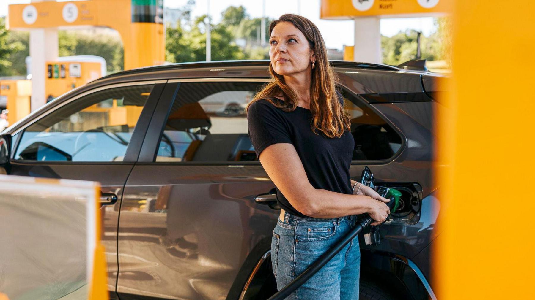 Stock photo shows a woman filling up her car with petrol at a station with yellow pumps