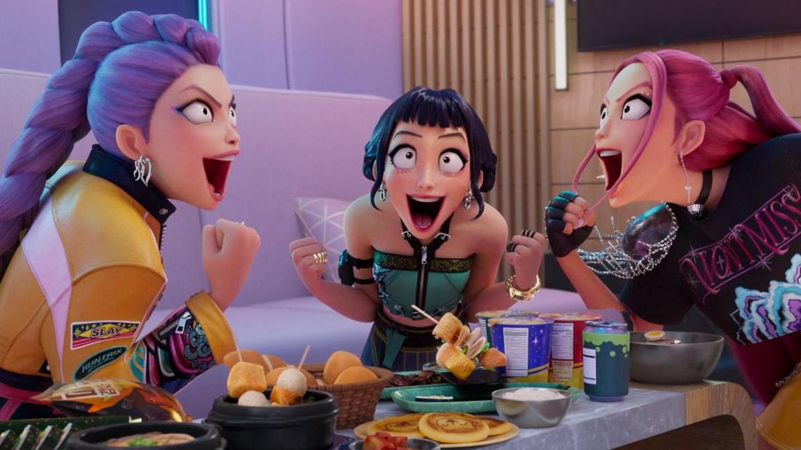 The three main characters in the Netflix animated movie Kpop Demon Hunters sit at a table full of food and celebrate.