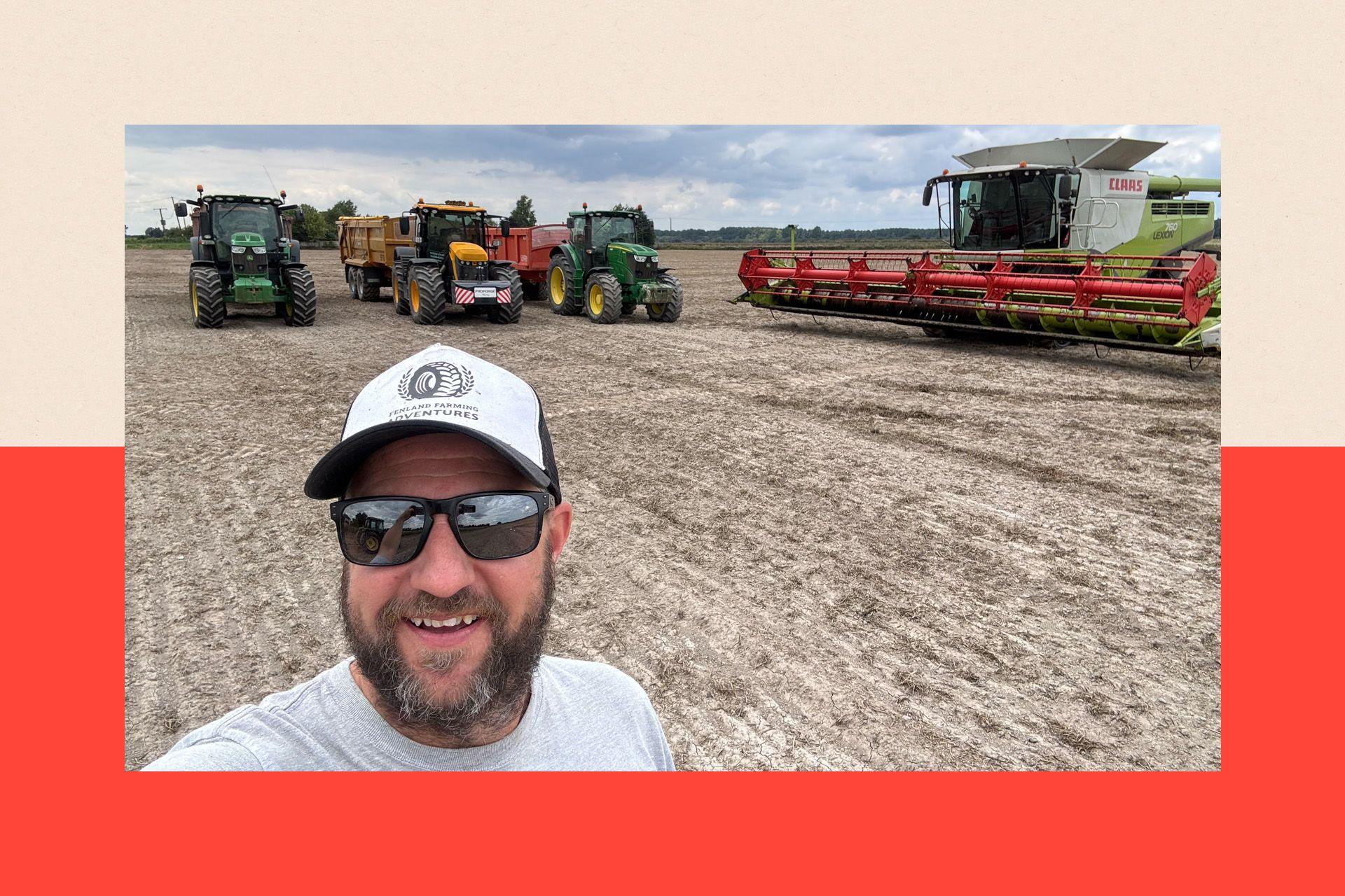 A man in a baseball cap and glasses in a dried out field. It is a selfie. There is farming equipment in the background.
