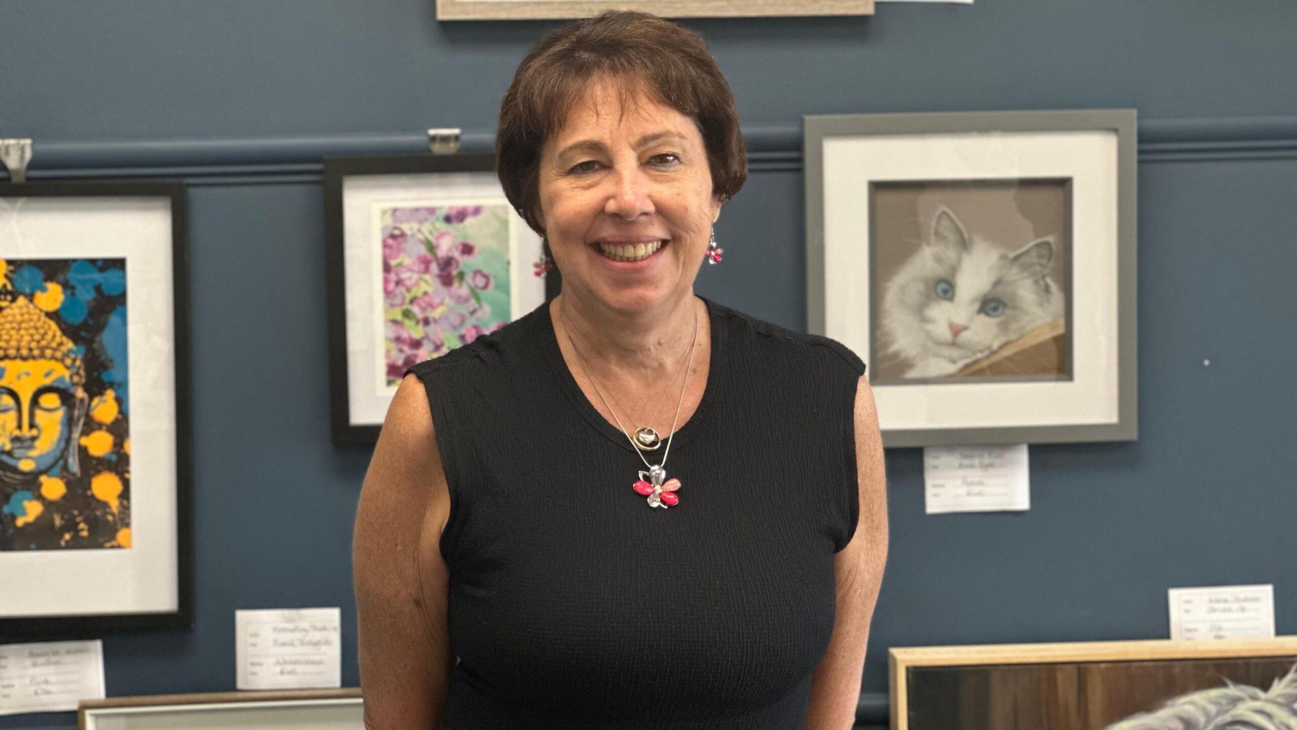 Dr Nicola Fox is stood, smiling, with a gallery of art behind her