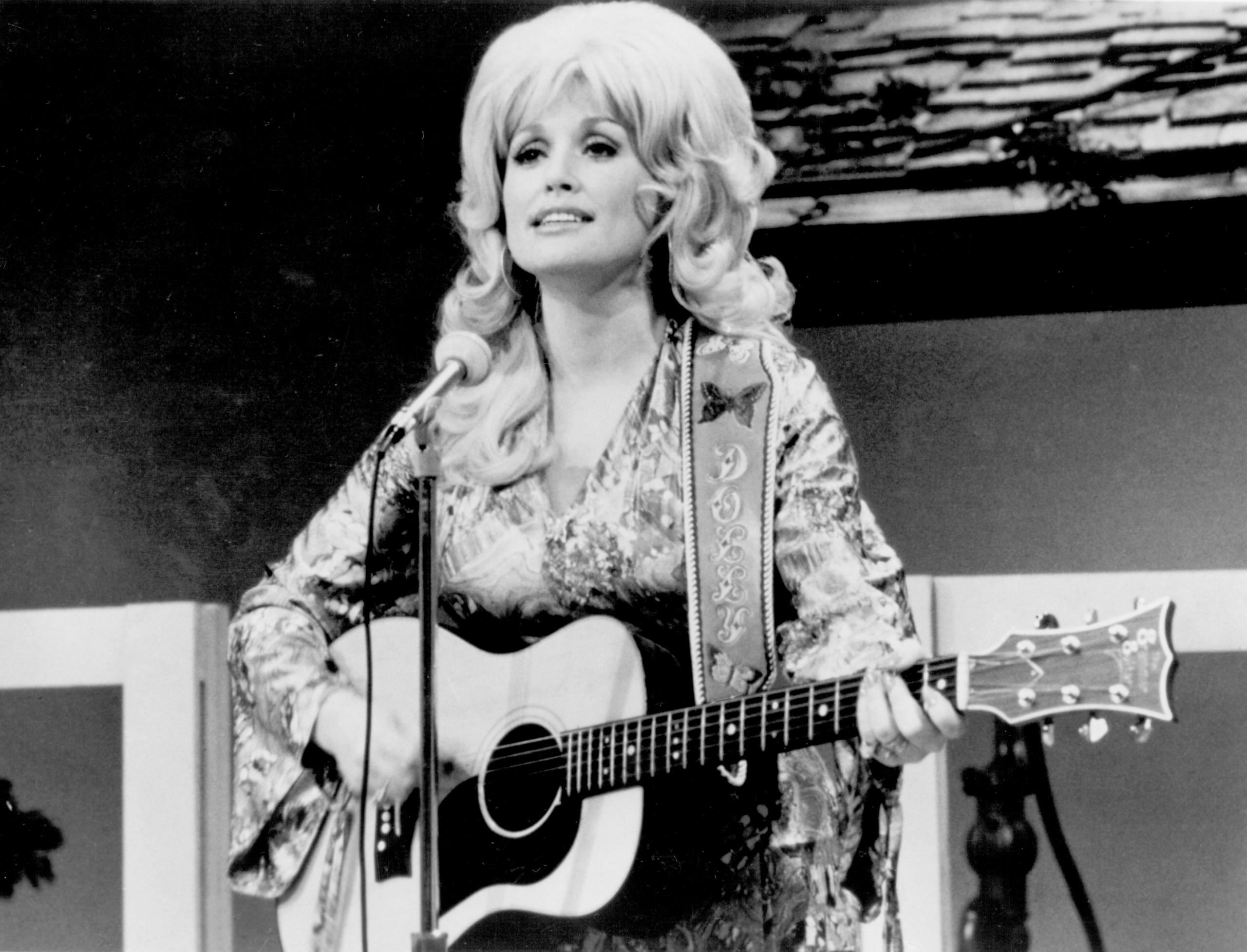 Black and white image of Dolly Parton on stage with a guitar