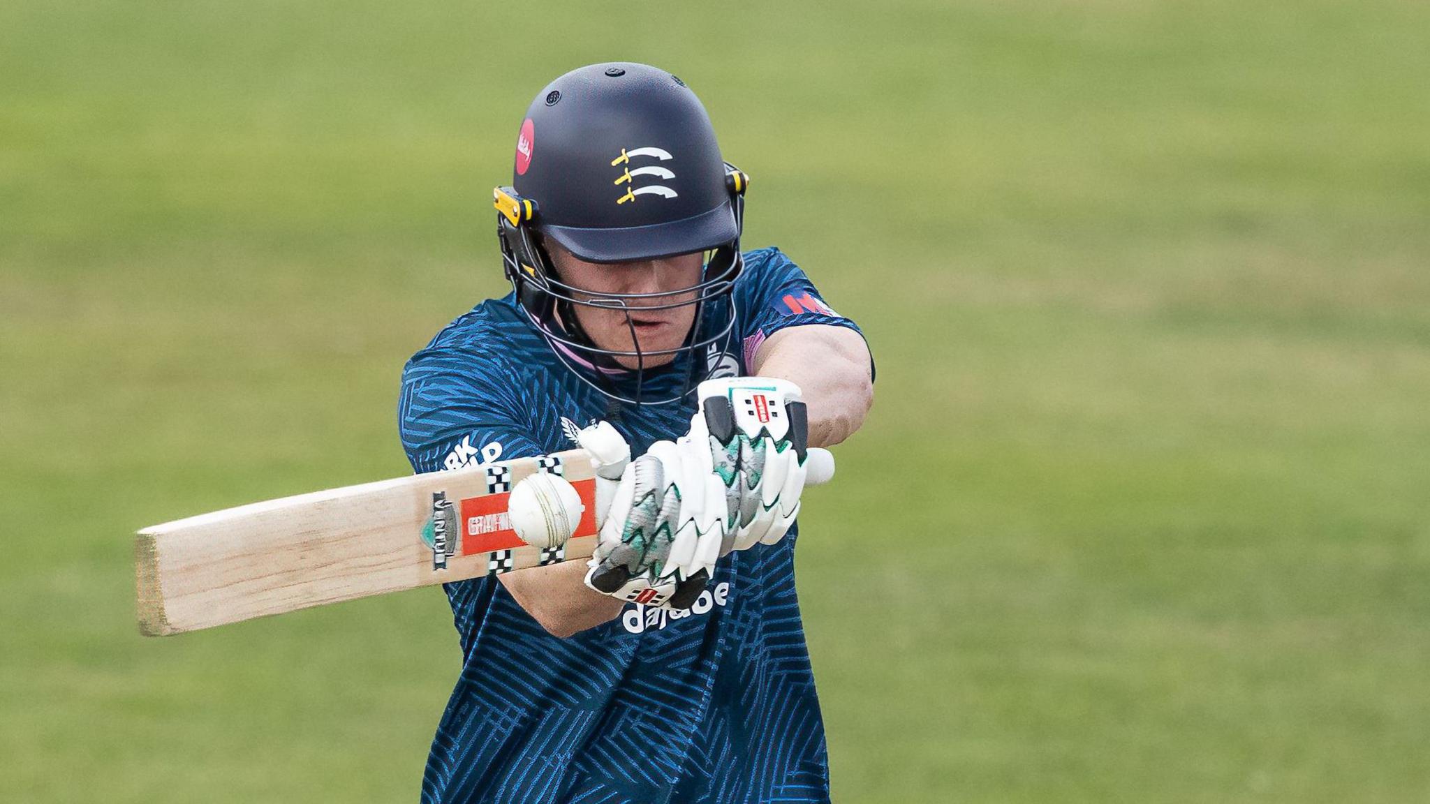 Ben Geddes hits a shot for Middlesex against Derbyshire in the One-Day Cup while wearing a dark blue top and helmet