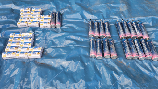 Large pile of black cannisters on a blue tarpaulin in a field with a spade next to it.