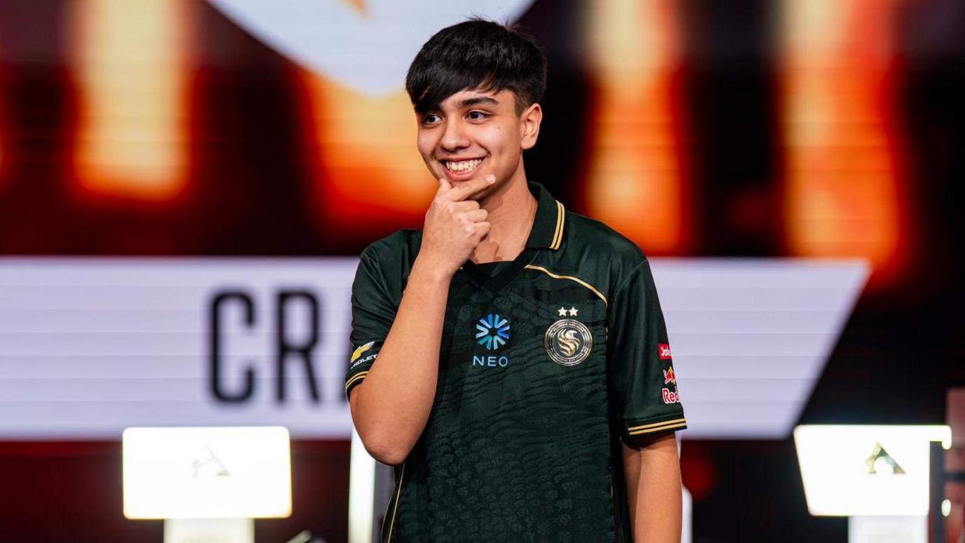 Jaime "Craime" Bustos stands on-stage, smiling, his hand held up to his chin, as he is announced as the winner of the EWC's Street Fighter 6 contest.