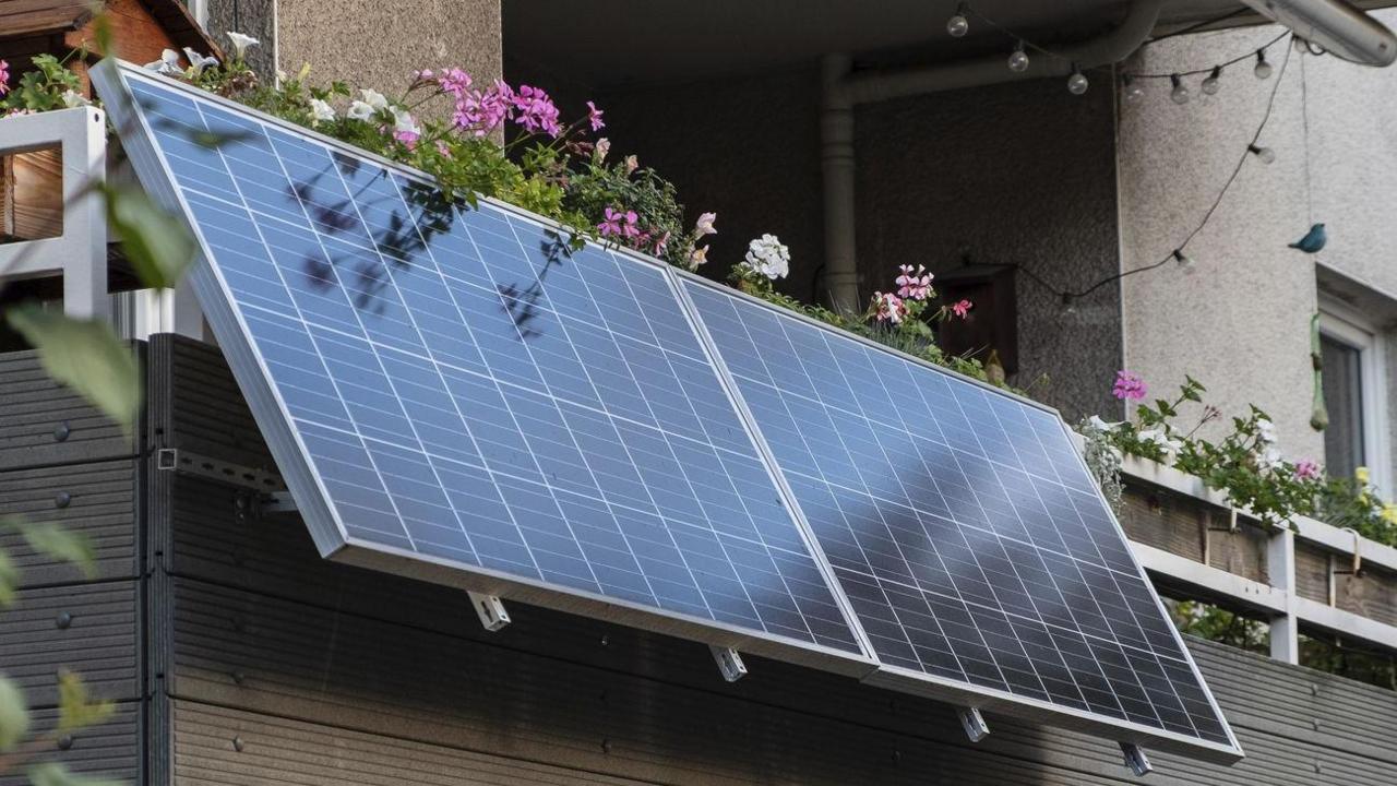 A solar panel hanging on a balcony, which also contains plants and flowers.