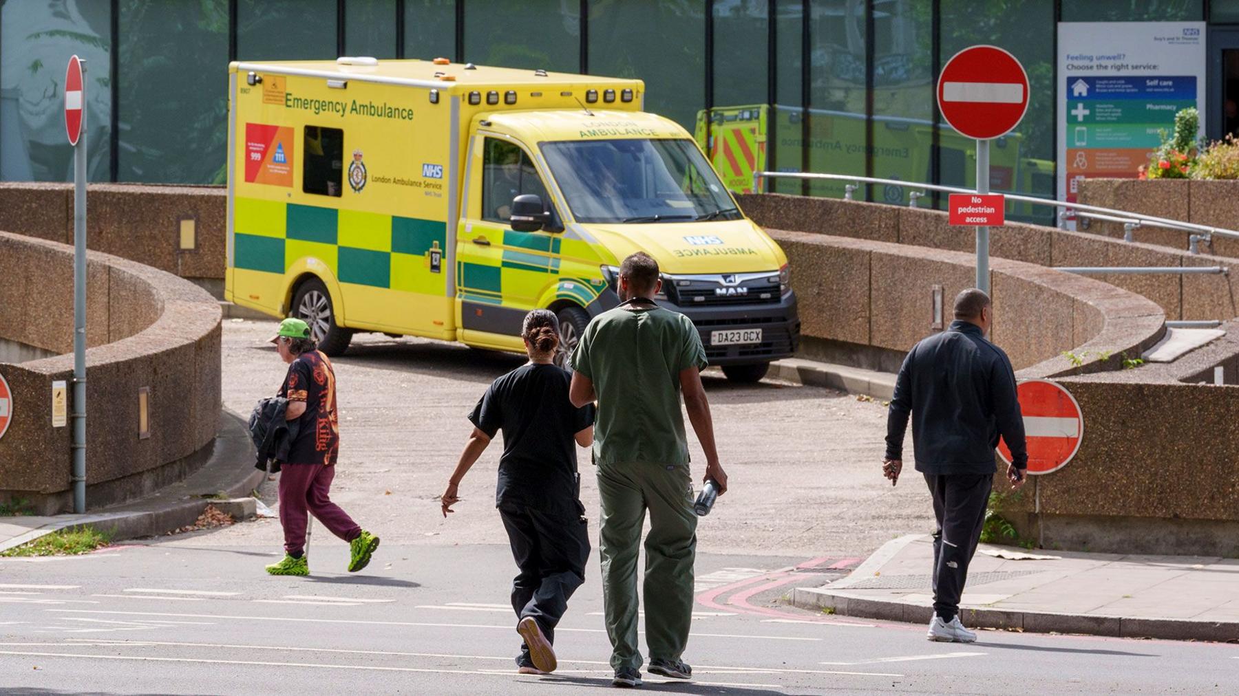 A yellow ambulance with the words Emergency Ambulance parked outside a hospital emergency department