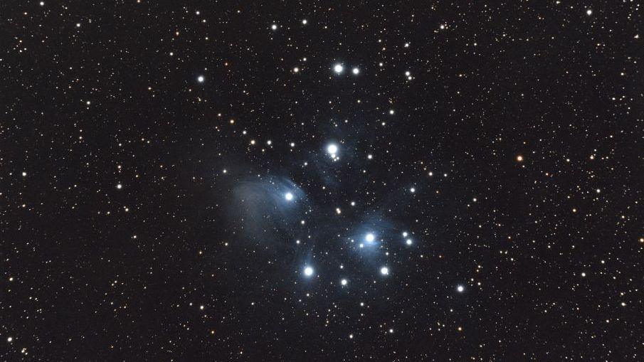 A group of stars shine bright white in the middle of starry black night sky.