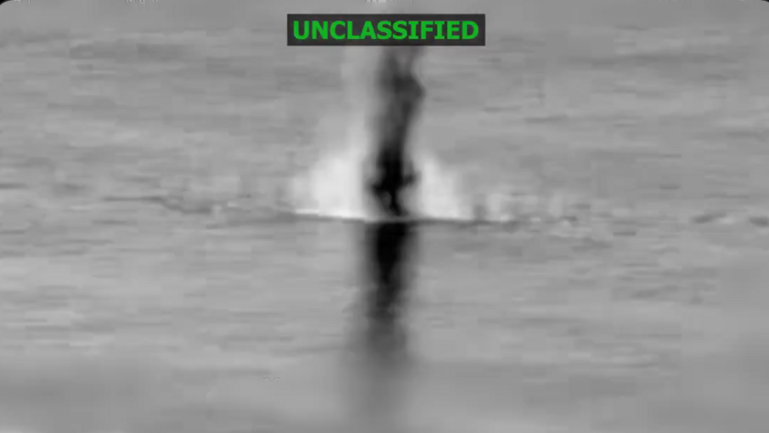 Screenshot from black and white video showing a boat being blown up in ocean with "unclassified" written across the top of the image