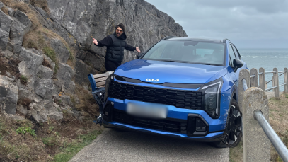 Canberk Beker by a blue Kia Sportage jammed between a fencepost and bench. His arms are apart and he is wearing a black body warmer