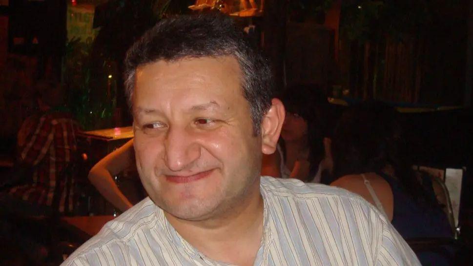 Saad al-Hilli smiles in a striped cream and light blue shirt. A busy night time scene is visible behind him.