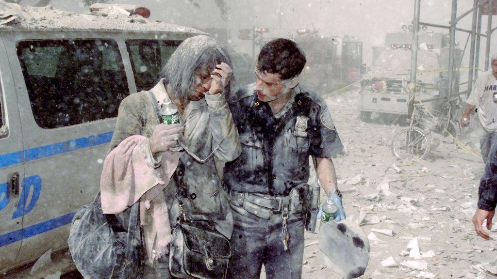 A police officer helps a distraught woman as ash and debris cover the area following the collapse of 1 World Trade Center on 11 September 2001