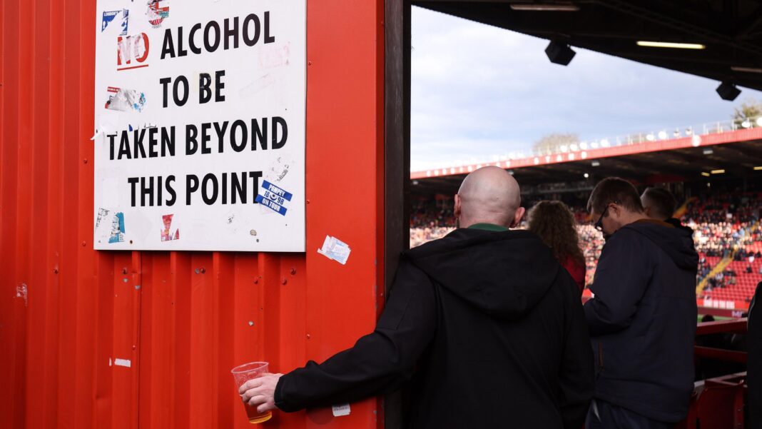 Burnham brands ban on football fans drinking alcohol in stands as ‘discrimination’ A football fan holds his pint of beer beneath a sign instructing that no alcohol should be taken beyond this point so he can continue to watch the match. The fan has his back to the camera and is wearing a dark-coloured jacket.