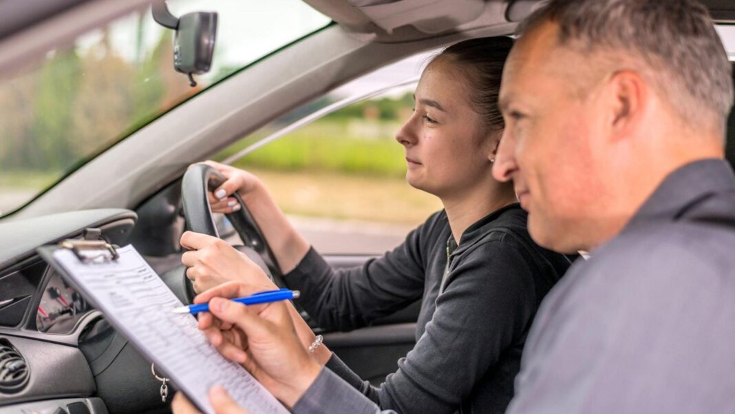 A young woman sitting her driving test. A male instructor is marking her on a clipboard