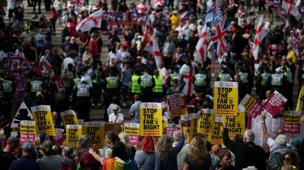 Protesters holding 'Stop the far right' posters with anti-migrant protesters waving St George and union flags on the steps beyond a line of police